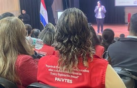 Mujer con chaqueta roja en auditorio, mientras otra habla desde un podio en un evento sobre protección infantil.