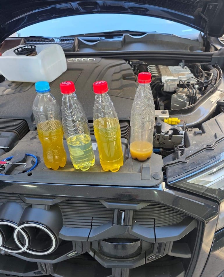 Compartimento del motor con botellas de líquidos de varios colores, capó abierto en un ambiente exterior.