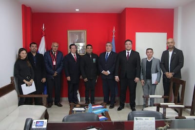 Grupo de ocho personas vestidas formalmente, en un ambiente interior, dialogando sobre integración fronteriza con rostros serios y atentos.