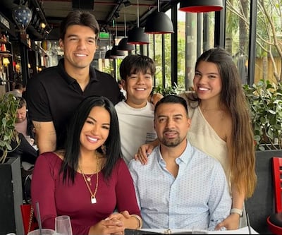 Julio César Cáceres en camisa blanca, acompañado de mujeres en vestido rojo y top beige, y dos niños felices en un ambiente iluminado.