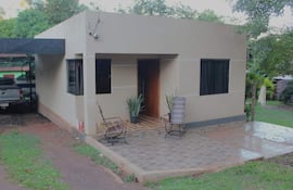 Vivienda unifamiliar con sillas de mimbre frente a un garage, camioneta plateada estacionada al lado.