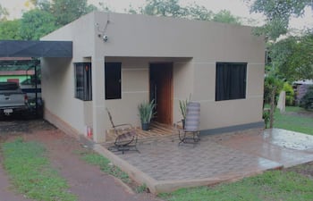 Vivienda unifamiliar con sillas de mimbre frente a un garage, camioneta plateada estacionada al lado.