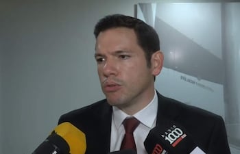 Alejandro Aguilera, vestido con traje oscuro y corbata, habla serio rodeado de micrófonos de prensa en un entorno formal.