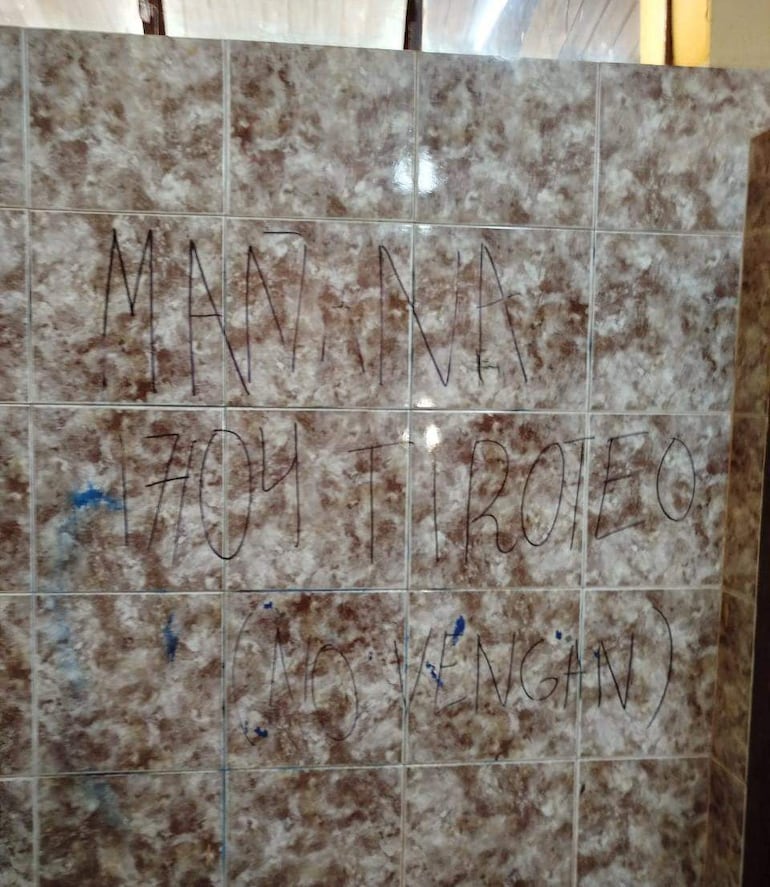 Mensaje escrito a mano en azulejos que advierte sobre un tiroteo, sin personas visibles en el interior.
