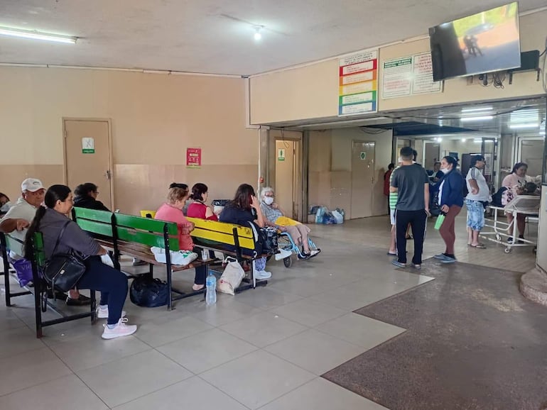 Diez personas en el interior del hospital; algunos pacientes con mascarillas y una mujer en silla de ruedas en un ambiente tranquilo.