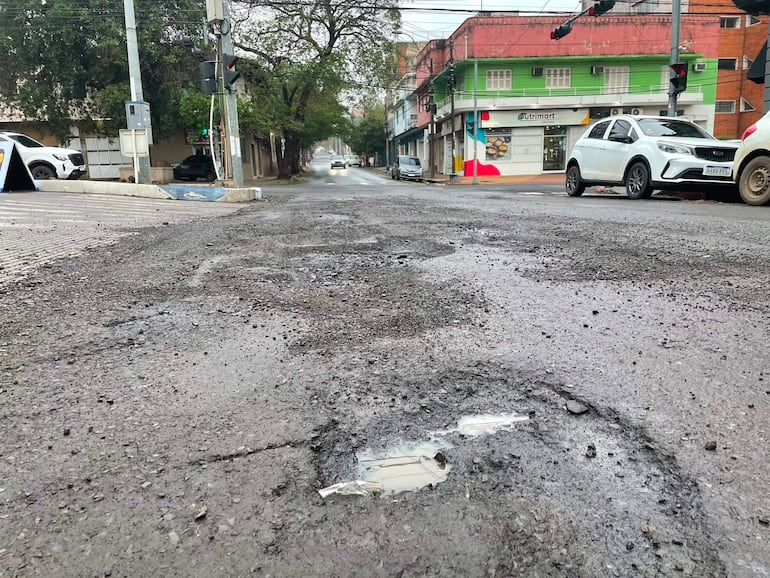 Calle de Asunción con pavimento deteriorado, semáforo verde y edificios coloridos, sin personas visibles.