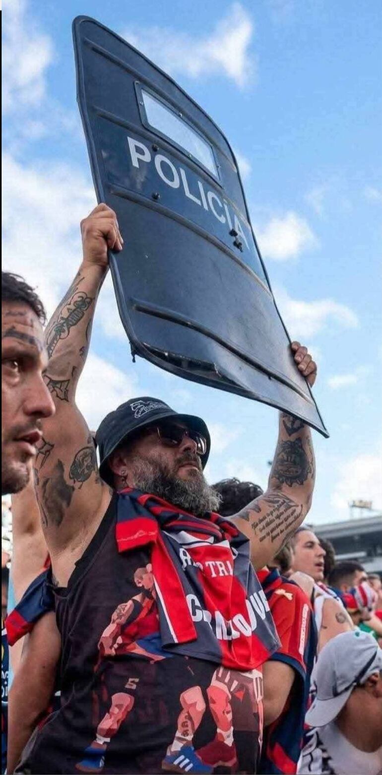 El barrabrava ahora detenido exhibe en las graderías el escudo que se le quitó a un oficial de la Policía.