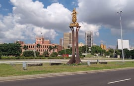 Estatua dorada de figura femenina sobre pedestal, Palacio de López al fondo, ambiente tranquilo y cielo parcialmente nublado.