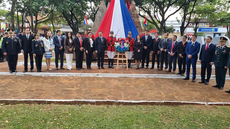 Grupo de personas vestidas formalmente y guardias en uniforme rojo colocan ofrenda floral en ceremonia solemne al aire libre.