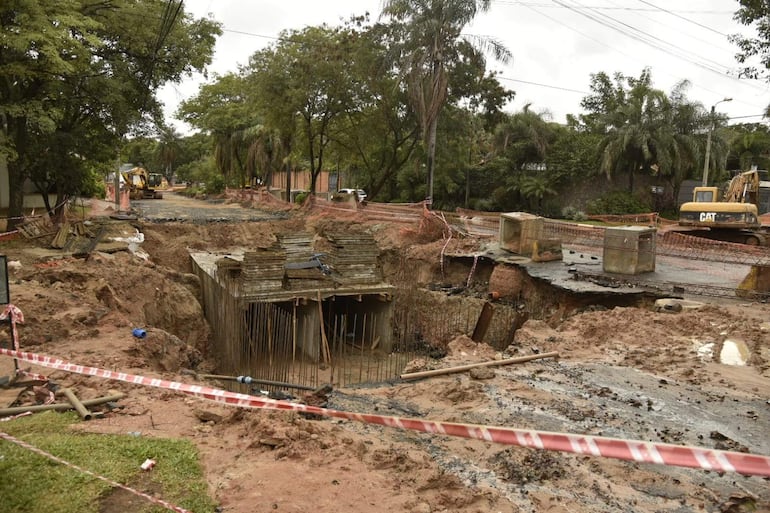 Maquinaria pesada marca CAT en obra de desagüe pluvial, rodeada de vegetación y cinta de advertencia.