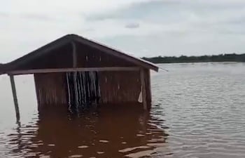 Construcción de madera semi-sumergida en agua, con cielo nublado, reflejando la situación de emergencia por inundaciones.