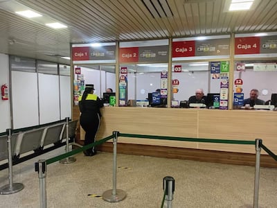 Policía en uniforme consulta en Caja 2, mientras tres personas mayores esperan conectadas a sus tareas, el entorno destaca por su iluminación.