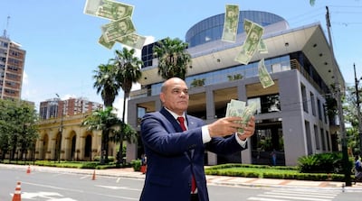 Basilio Núñez con traje oscuro y corbata roja, lanzando billetes al aire frente al edificio del Congreso.