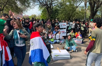 Jóvenes manifestantes sostienen carteles con mensajes de protesta, algunos aplauden, mientras otros escuchan con atención en un ambiente urbano.