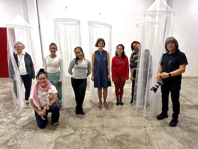 Grupo de ocho personas posando con sonrisas, en un ambiente contemporáneo, con variados atuendos, entre ellos un blazer, camisetas y un vestido azul.