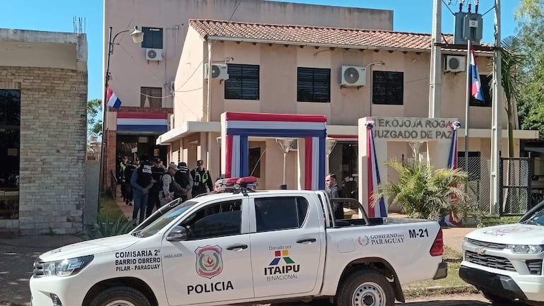 Policías en uniforme conversan frente al Juzgado de Paz, con un vehículo policial visible y decoraciones en colores de la bandera paraguaya.
