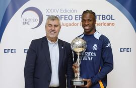 MADRID, 31/12/2024.- El delantero brasileño del Real Madrid Vinicius jr. (d), acompañado por el presidente de la Agencia EFE, Miguel Ángel Oliver (i), posa con el Trofeo EFE al Mejor Jugador Iberoamericano de Fútbol antes de participar en el entrenamiento realizado este martes, último día del año, en Valdebebas.Tras regresar el lunes al trabajo después del descanso navideño, el Real Madrid, que el viernes visita al Valencia en un partido pendiente de la duodécima jornada y que fue aplazado por la dana, se entrena este martes a puerta abierta, con acceso único para los socios del club. EFE