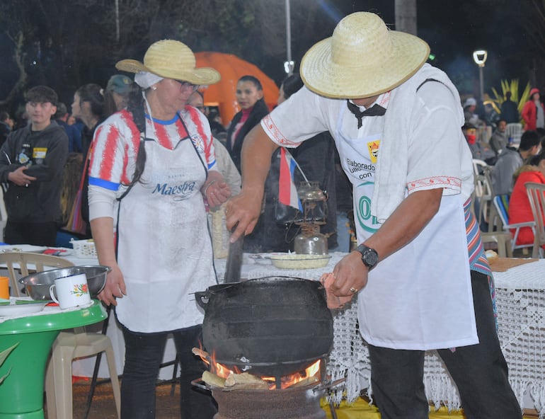 Hombre en delantal blanco y mujer en camiseta colorada cocinando en ambiente festivo durante el Festival del Reviro.