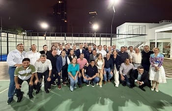 Grupo de personas vestidas formalmente, incluyendo a Santiago Peña, sonriendo en un evento exterior bien iluminado.