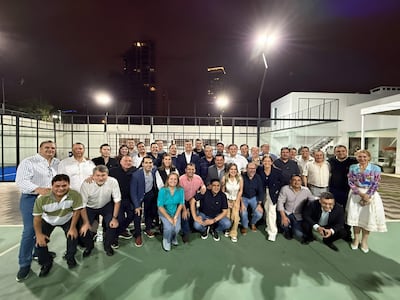 Grupo de personas vestidas formalmente, incluyendo a Santiago Peña, sonriendo en un evento exterior bien iluminado.