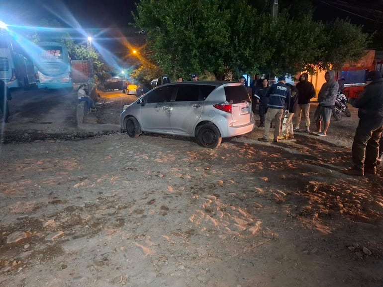 Varias personas, incluidas fuerzas de seguridad con chaquetas de 'Policía', se reúnen alrededor de un vehículo blanco en la noche.
