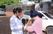 Profesional de salud en bata blanca interactúa con mujer mayor en abrigo rosa y niña en el exterior del hospital.