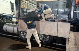 Hombres con uniformes oscuros de PRF levantan bloques de carga junto a un camión en ambiente nocturno.