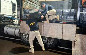 Hombres con uniformes oscuros de PRF levantan bloques de carga junto a un camión en ambiente nocturno.