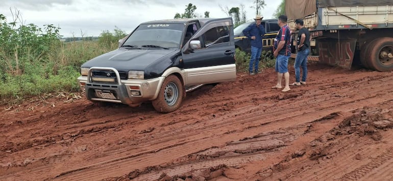 Cuatro personas en ambiente rural, observando un vehículo todoterreno negro semiatrapado en barro, bajo la lluvia.
