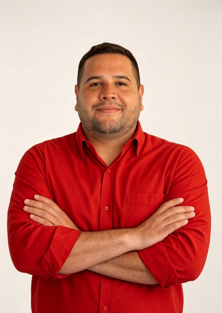 Derlis Maidana, con camisa roja y sonrisa amable, posa de pie con los brazos cruzados en un fondo claro.