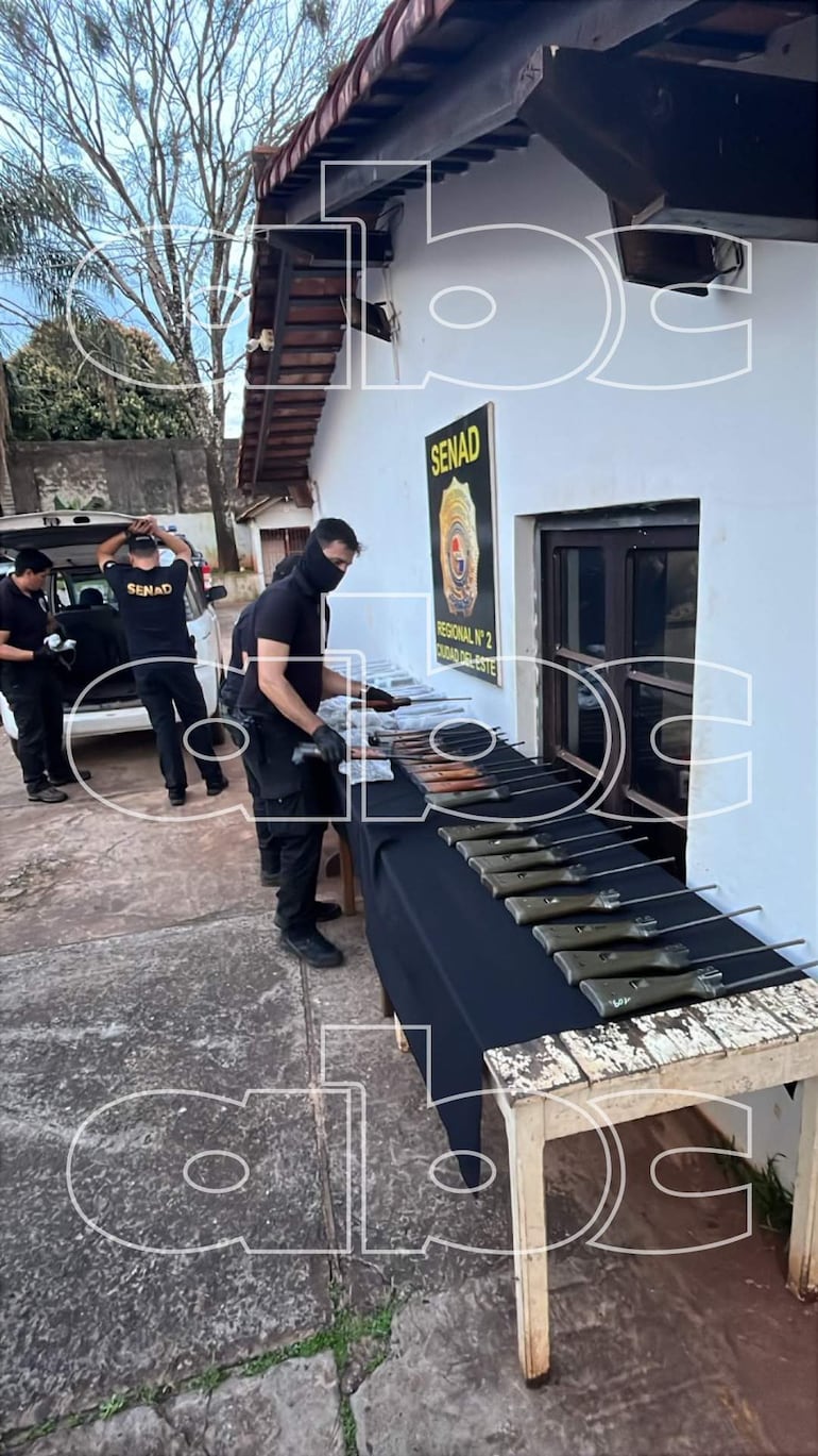 Cuatro agentes en vestimenta oscura y guantes, manipulando armas junto a un vehículo bajo un ambiente exterior.