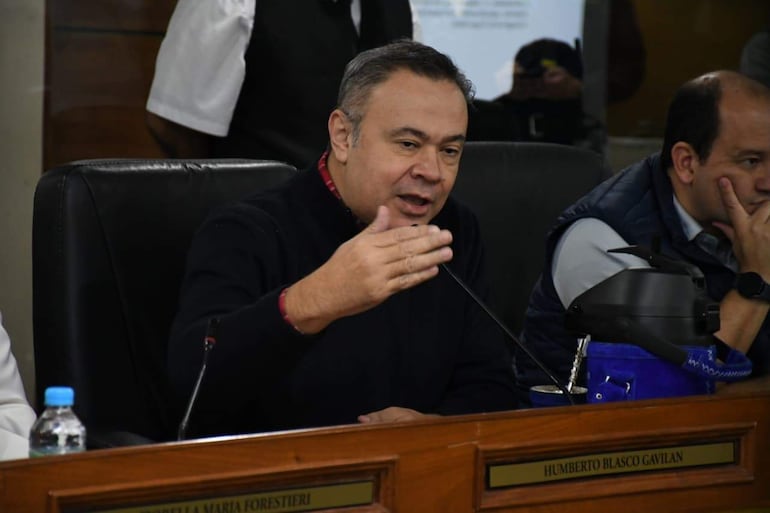 Felix Ayala, en suéter negro y camisa de cuadros rojos, habla con gestos, mientras Humberto Blasco lo observa sentado.