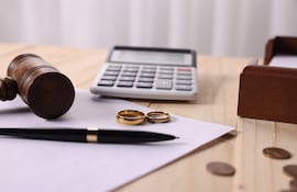 Escena de oficina con mazo de juez, dos anillos de boda y calculadora sobre una mesa, sin personas visibles.
