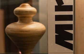 Un jarrón de madera en vitrina con diseño espiral, y cartel que dice 'SU MIRÁS' con letras rojas y negras.