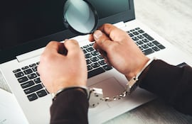 manos de hombres esposadas, sosteniendo una lupa sobre el teclado de una computadora