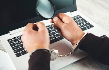 manos de hombres esposadas, sosteniendo una lupa sobre el teclado de una computadora