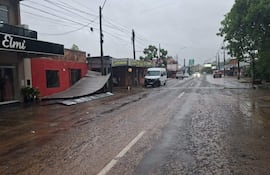 Establecimiento 'Elmi' en un día lluvioso, con toldo metálico caído, vehículos en movimiento y charcos en la calle.