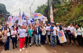 Soledad Núñez y Humberto Blasco marchan con camisetas blancas y sonrisas, rodeados de un grupo colorido en ambiente urbano.