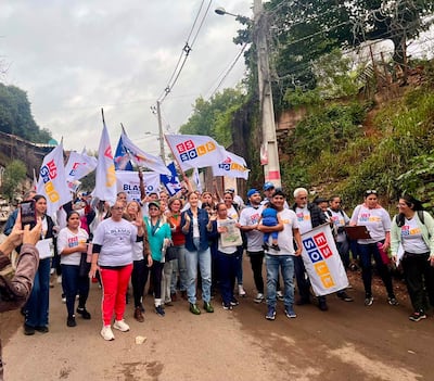 Soledad Núñez y Humberto Blasco marchan con camisetas blancas y sonrisas, rodeados de un grupo colorido en ambiente urbano.