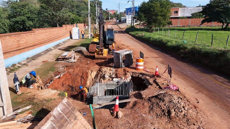 Tres trabajadores en el sitio de construcción, uno agachado con chaleco reflectante, rodeados de maquinaria y materiales de construcción.