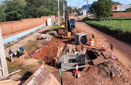 Tres trabajadores en el sitio de construcción, uno agachado con chaleco reflectante, rodeados de maquinaria y materiales de construcción.