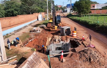 Tres trabajadores en el sitio de construcción, uno agachado con chaleco reflectante, rodeados de maquinaria y materiales de construcción.