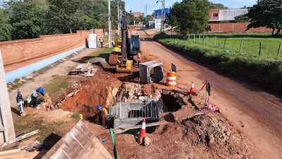 Tres trabajadores en el sitio de construcción, uno agachado con chaleco reflectante, rodeados de maquinaria y materiales de construcción.