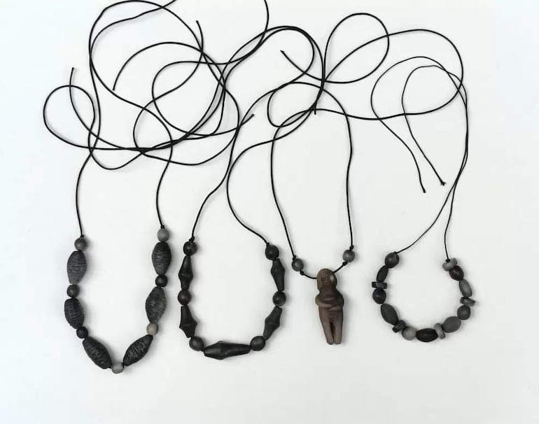 Cuatro collares sobre superficie blanca, destacando cuentas oscuras y una figura humana en el segundo collar.