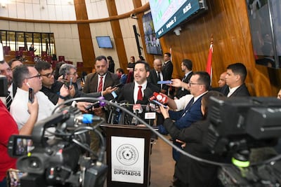 Raúl Latorre con traje oscuro y corbata roja, rodeado de periodistas con micrófonos en un entorno legislativo moderno.