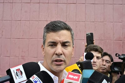 Santiago Peña con expresión seria sostiene un micrófono, rodeado de periodistas en un ambiente de cobertura mediática.