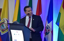 Félix Sosa en traje oscuro con corbata roja, de pie frente a un podio, discurso en un ambiente iluminado en azul.