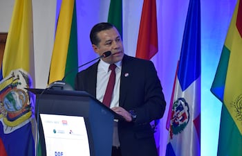 Félix Sosa en traje oscuro con corbata roja, de pie frente a un podio, discurso en un ambiente iluminado en azul.