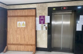 Área interior frente a ascensor en obra, con pared de madera y señales de advertencia de peligro.