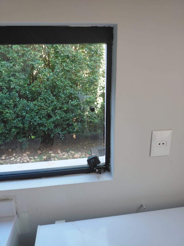 Vista interior de una casa con luz natural y ventana abierta, sin personas visibles y un posible dispositivo de seguridad en primer plano.